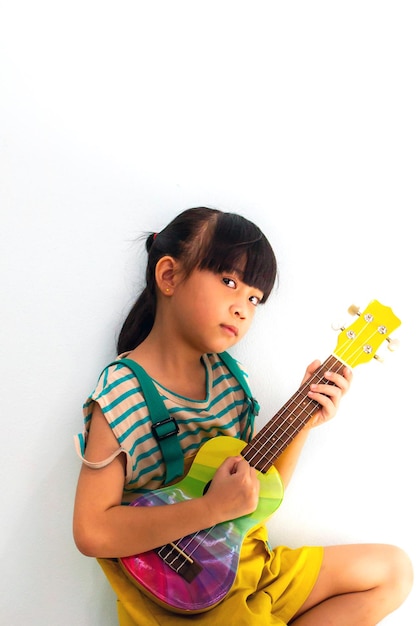 Menina bonitinha tocando ukulele no fundo branco