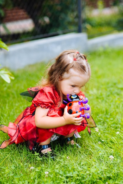 Foto menina bonitinha vestida com um vestido longo vermelho brincando e se divertindo em um gramado verde