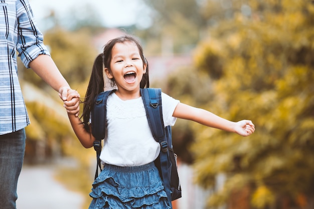 Menina bonito aluno asiático com mochila segurando a mão da mãe e ir para a escola