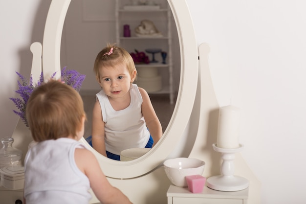 Menina bonito, assistindo seu reflexo em um quarto branco com um espelho redondo