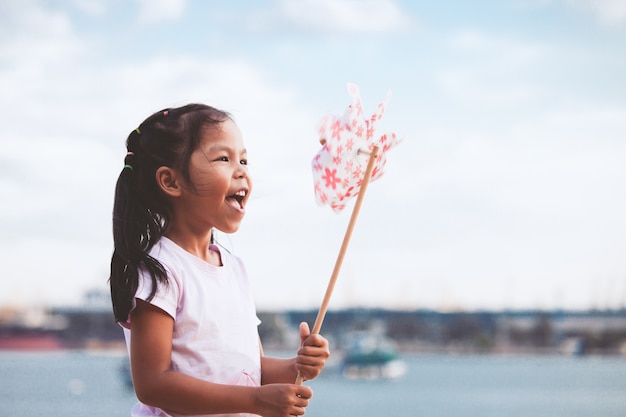 Menina bonito criança asiática brincando com turbina de vento de brinquedo na praia com felicidade