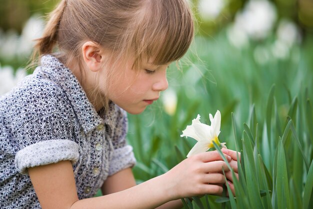 Menina bonito criança pensativa ao ar livre com narciso branco no verão ensolarado ou dia de primavera no verde turva