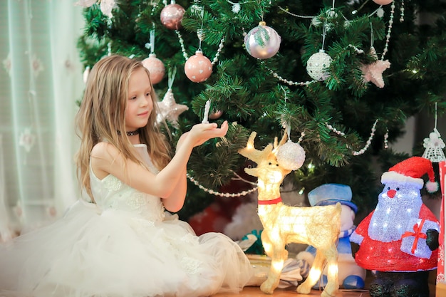 Menina bonito perto da árvore de natal. crianças sob a árvore de natal com caixas de presente.