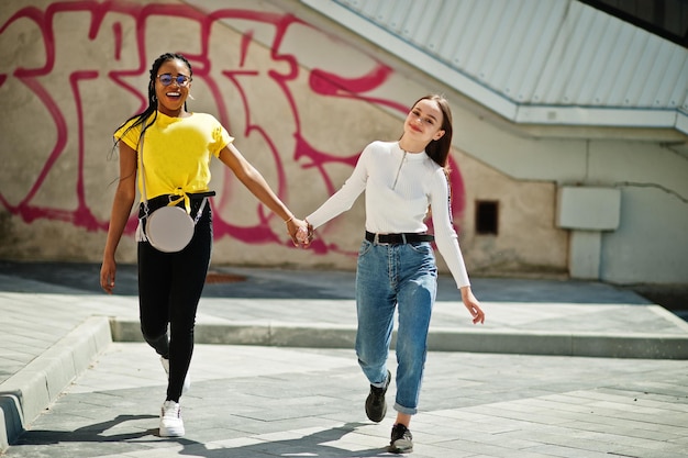 Menina branca caucasiana e negro afro-americano juntos contra a parede do graffiti. Unidade mundial, amor racial, compreensão na tolerância e cooperação na diversidade racial.