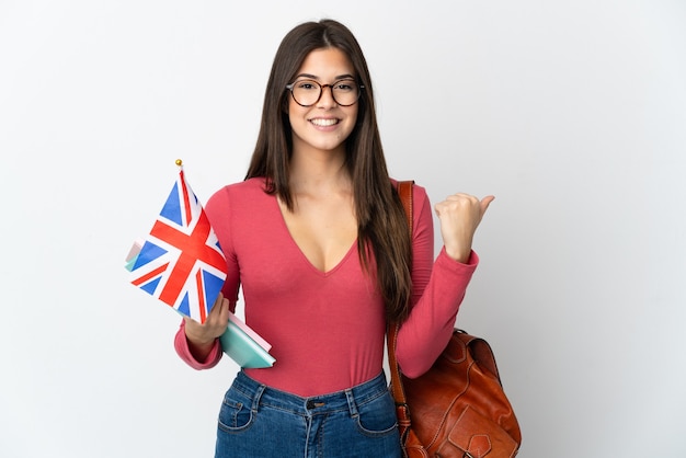 Menina brasileira adolescente segurando uma bandeira do Reino Unido isolada no branco apontando para o lado para apresentar um produto