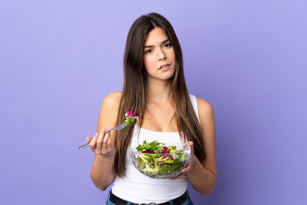 Menina brasileira adolescente segurando uma salada sobre fundo roxo isolado