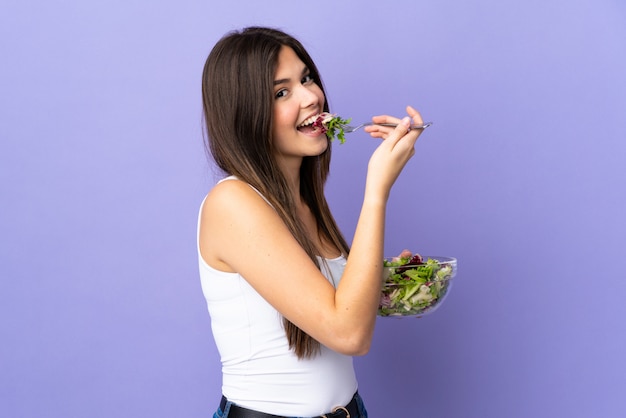 Menina brasileira adolescente segurando uma salada sobre parede roxa isolada