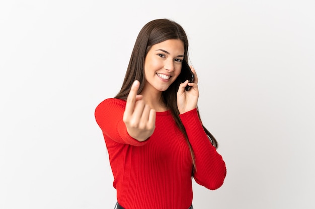 Menina brasileira adolescente usando telefone celular sobre fundo branco isolado fazendo gesto próximo