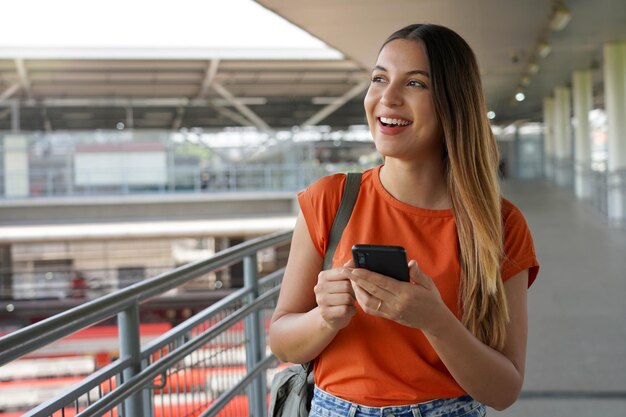 Foto menina brasileira caminhando na estação de trem segurando um smartphone em são paulo, brasil