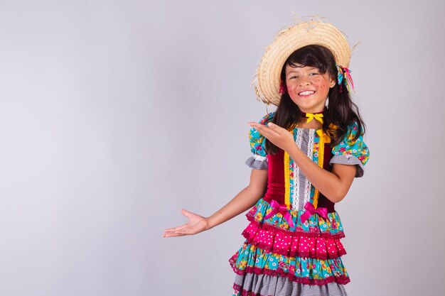 Menina brasileira com roupas de festa junina apresentando algo na propaganda de produto lateral