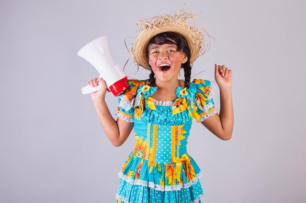 Foto menina brasileira em roupas de festa junina segurando megafone anunciando