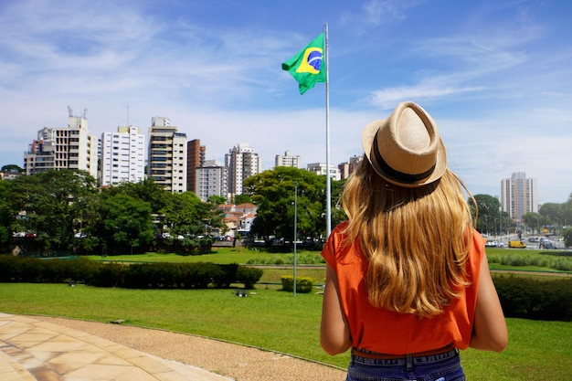 menina brasileira olhando para a bandeira nacional com a paisagem urbana de São Paulo no fundo Brasil