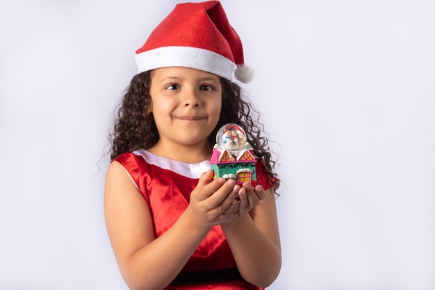 Menina brasileira vestida com fantasia de natal segurando globo de neve