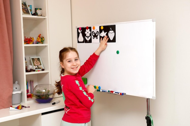 menina brinca na escola em casa pendurando fotos no quadro