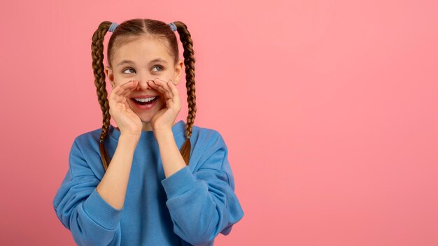 Foto menina brincalhona com as mãos para o rosto em fundo rosa