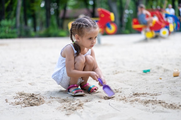 Menina brincando caixa de areia parque infantil cavar areia pá construir figura de areia dia de verão caucasiana criança 5 anos divertir-se ao ar livre