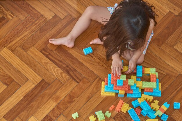 Menina brincando com blocos no chão de madeira no quarto dela
