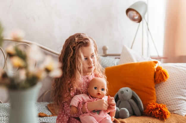 Menina brincando com boneca na cama no quarto das crianças