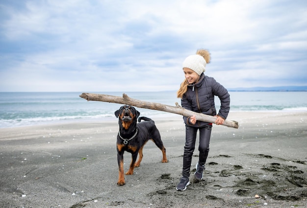 Menina brincando com cachorro rottweiler em clima frio na praia