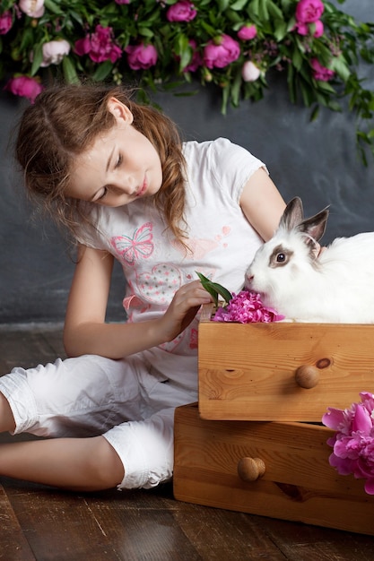 Menina brincando com coelho de verdade. Criança e coelhinho branco na Páscoa. Crianças e animais de estimação brincam. Diversão e amizade para animais e crianças.