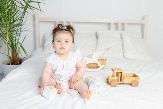 Menina brincando com cubos de brinquedo de madeira na cama em casa em uma sala iluminada o conceito de desenvolvimento da primeira infância