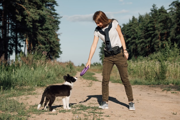 Menina brincando com filhote de cachorro border collie preto e branco no caminho da floresta