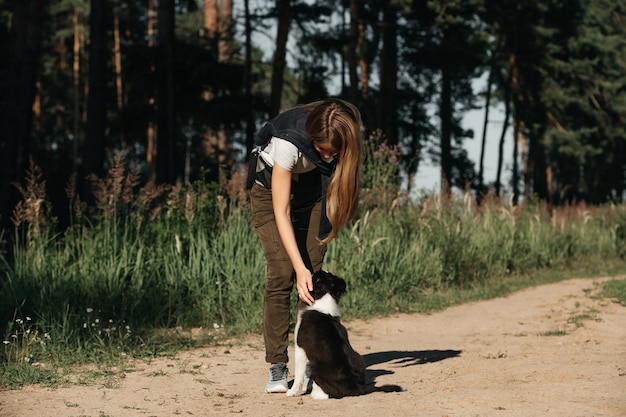Menina brincando com filhote de cachorro border collie preto e branco no caminho da floresta