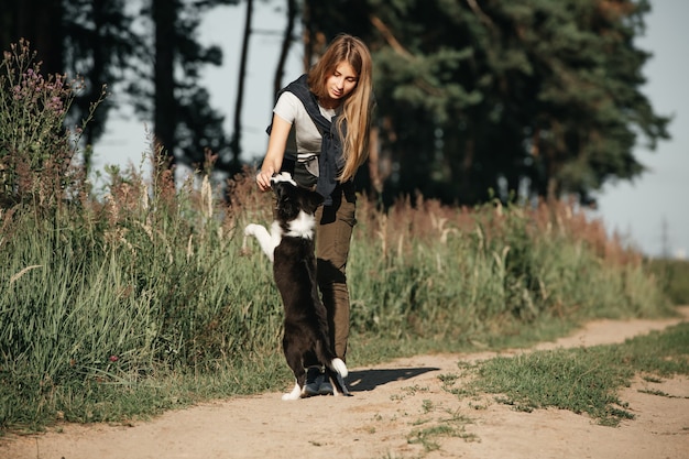 Menina brincando com filhote de cachorro border collie preto e branco no caminho da floresta