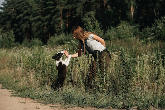 Menina brincando com filhote de cachorro border collie preto e branco no caminho da floresta