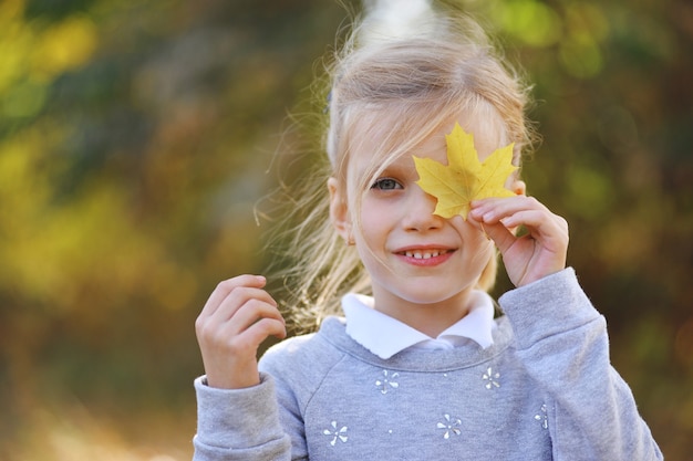 Menina brincando com folhas amarelas no parque outono
