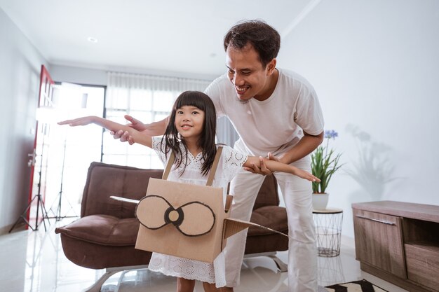 Menina brincando com o avião de brinquedo de papelão em casa com o pai