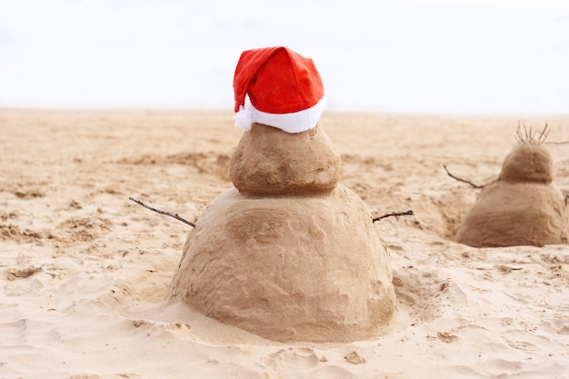 Menina brincando com um boneco de neve de areia de ano novo ou feliz natal na praia tropical de areia do oceano