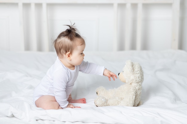 Menina brincando com um ursinho de pelúcia na cama em casa, o conceito de brincar e o desenvolvimento das crianças