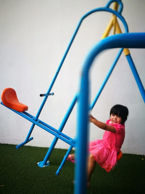 Foto menina brincando de balanço no playground contra a parede