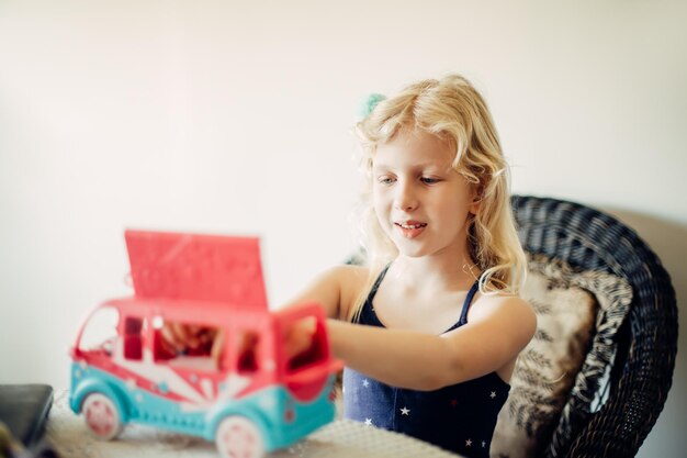 Foto menina brincando de carro de brinquedo ônibus com bonecas ativa criança pequena criança brincando sozinha em uma quarentena em casa