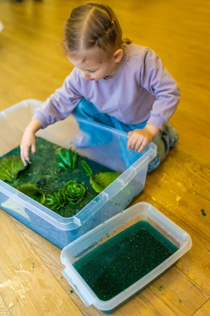 Menina brincando em pântano feito à mão de sementes de chia tingidas de verde com insetos, peixes e modelos de plantas