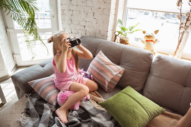 Menina brincando em um quarto em um estilo caseiro de pijama fofo e confortável tirando uma foto se divertindo