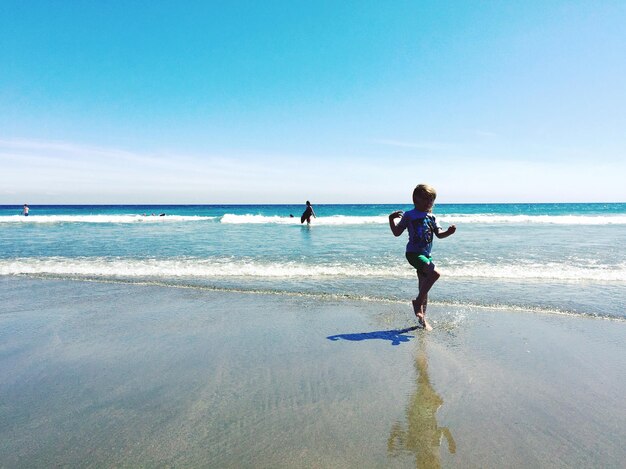 Foto menina brincando na praia contra o céu claro