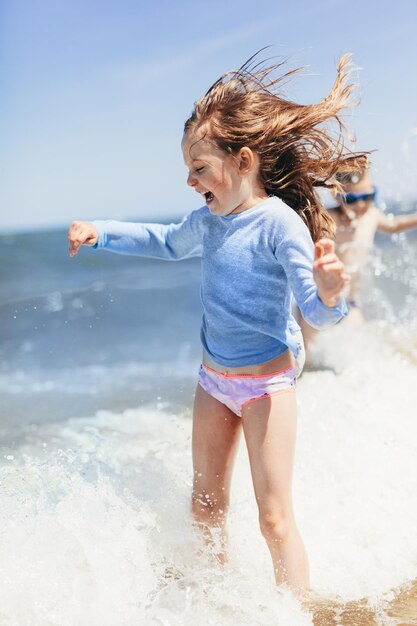 Menina brincando na praia em ondas nas férias de verão