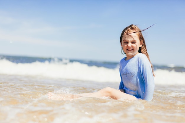 Menina brincando na praia em ondas nas férias de verão