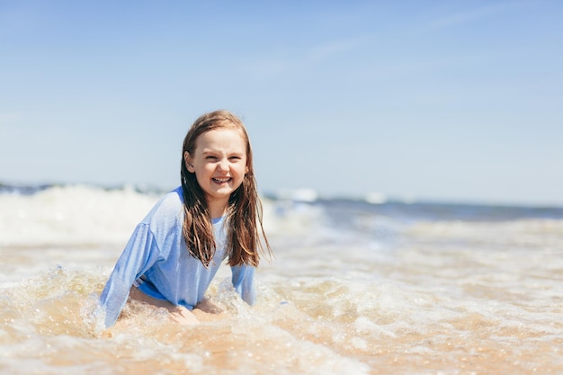 Menina brincando na praia em ondas nas férias de verão