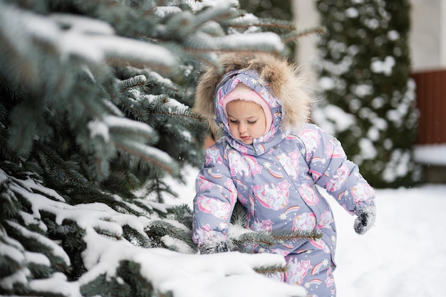 Menina brincar ao ar livre na neve perto da árvore de Natal no inverno