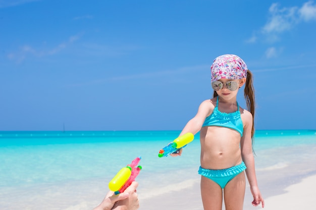 Menina brincar com a pistola de água na praia tropical