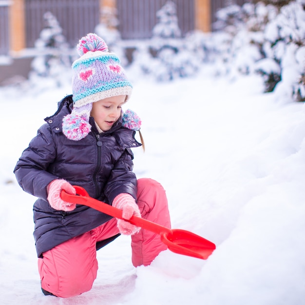 Menina brincar com neve pá em um dia de inverno