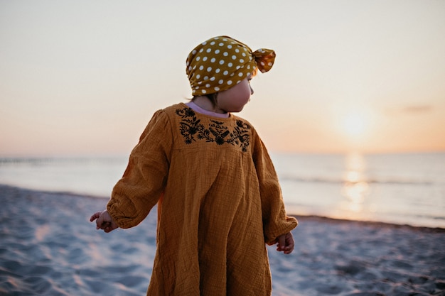 Menina caminhando na praia e se voltando para a água e o sol