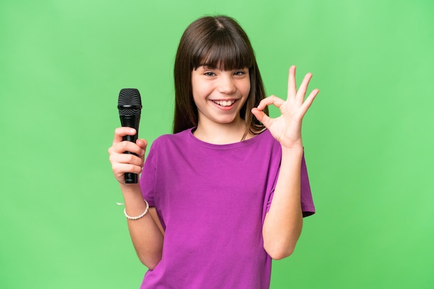 Menina cantora pegando um microfone sobre fundo isolado mostrando sinal de ok com os dedos