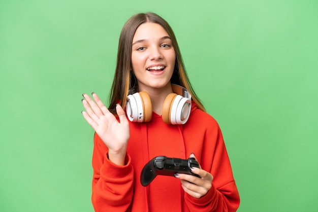 Menina caucasiana adolescente brincando com um controlador de videogame sobre fundo isolado, saudando com a mão com expressão feliz