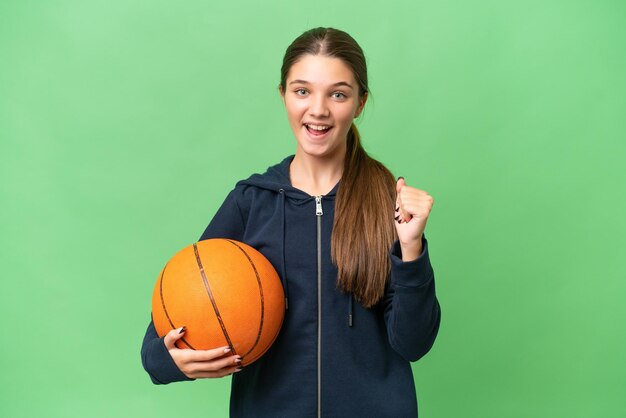 Menina caucasiana adolescente jogando basquete sobre fundo isolado comemorando uma vitória na posição de vencedor