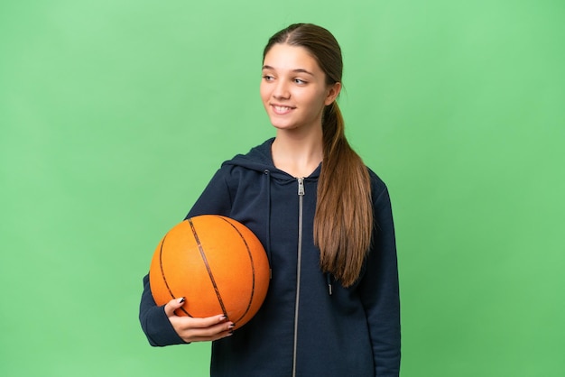 Menina caucasiana adolescente jogando basquete sobre fundo isolado, olhando para o lado e sorrindo