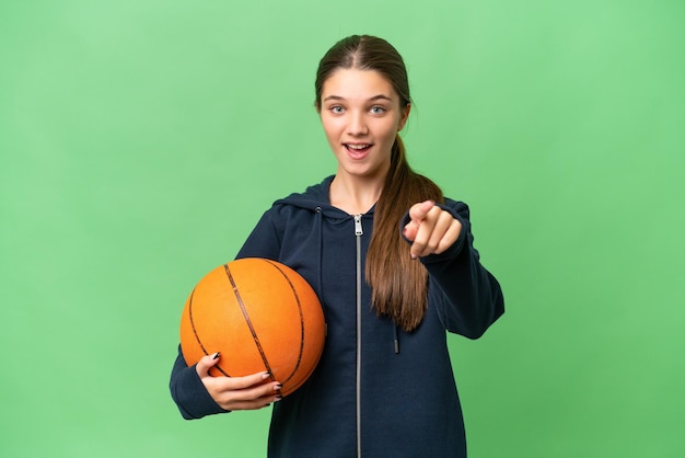 Menina caucasiana adolescente jogando basquete sobre fundo isolado surpreso e apontando para a frente